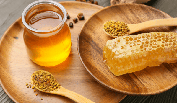 Miel de abejas en un recipiente, polen de abejas en una cuchara y un panal de miel